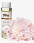 Koka Beauty body oil bottle with a pink peony flower on a white background