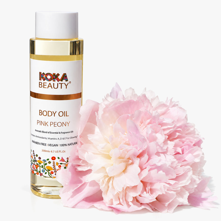 Koka Beauty Pink Peony Body Oil bottle beside a large pale pink peony bloom on white